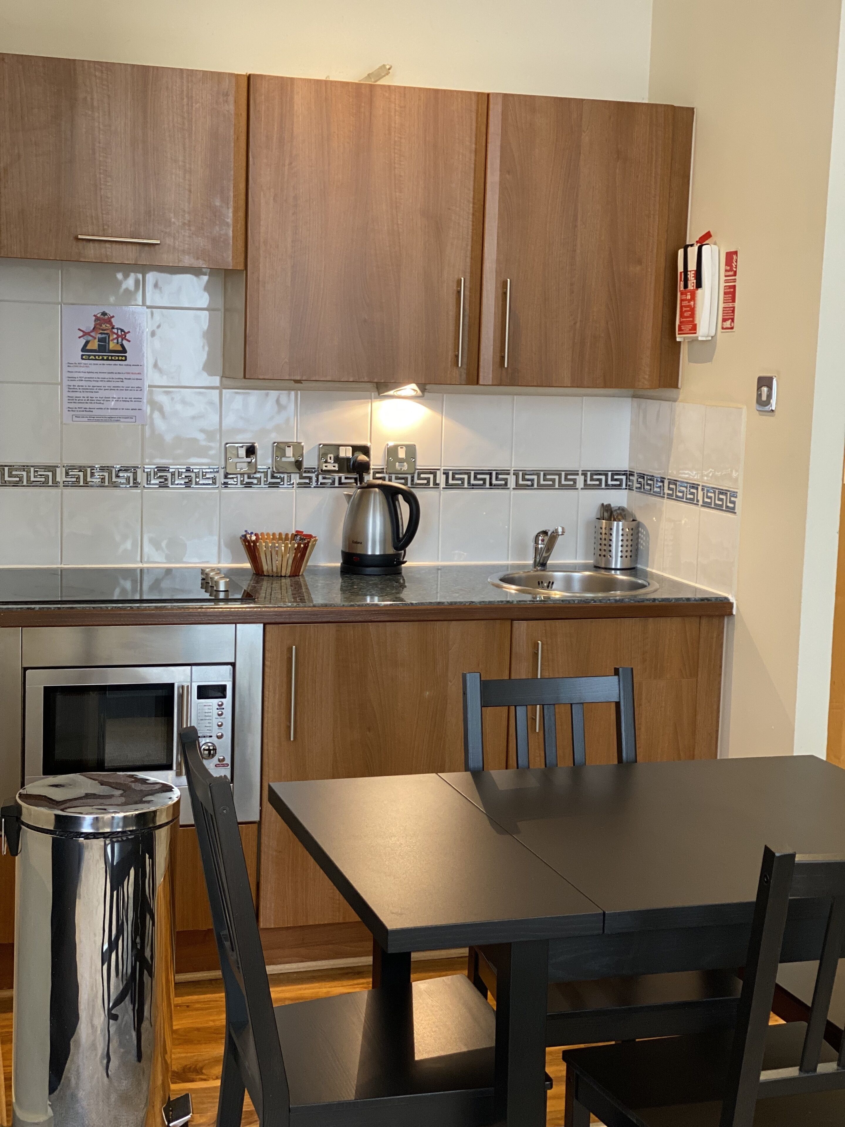 Una cocina con armarios de madera, microondas, hervidor y una mesa de comedor con sillas.