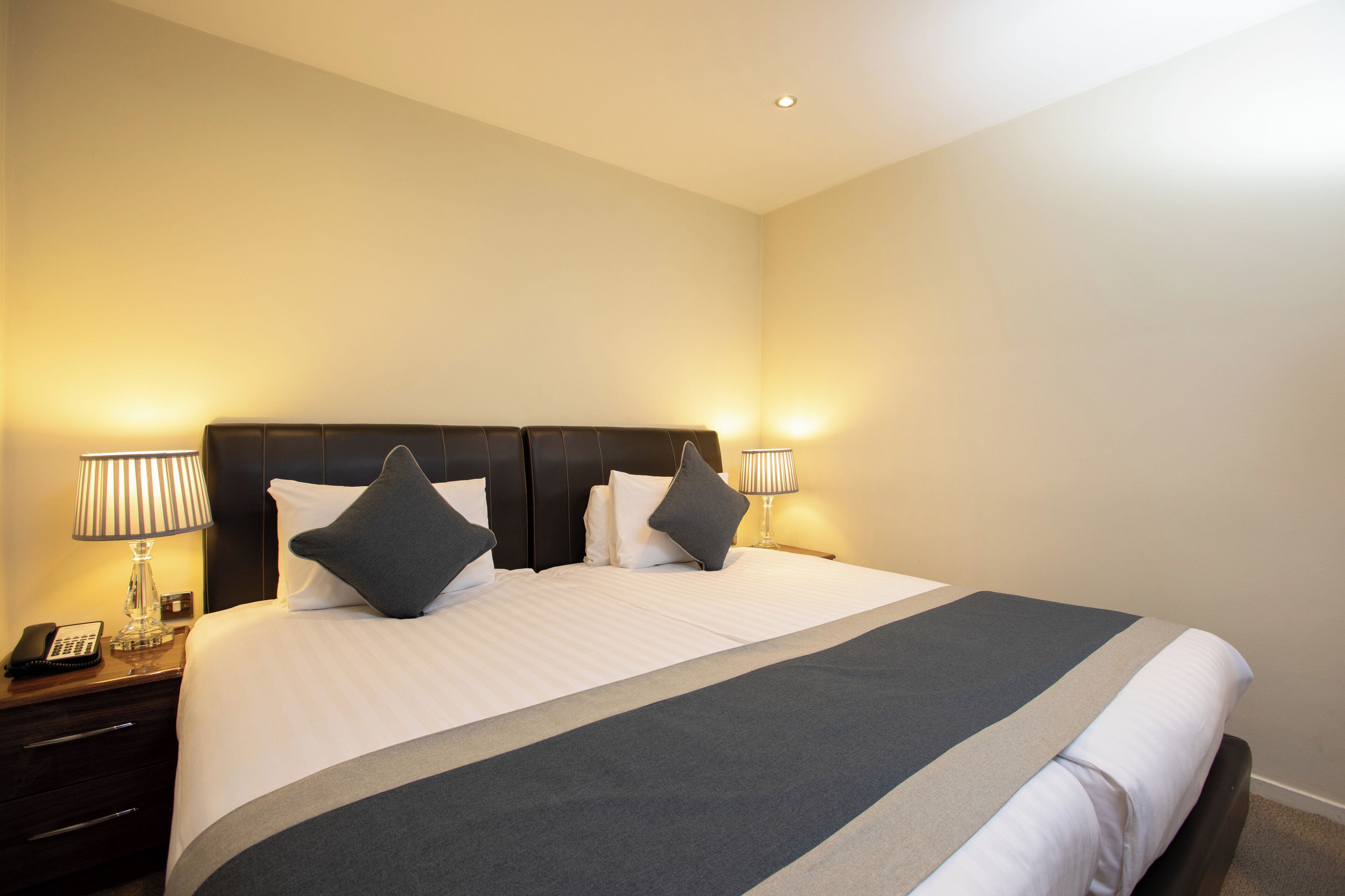 A hotel room with a large bed, two bedside lamps, a nightstand with a phone, and a wall-mounted light.