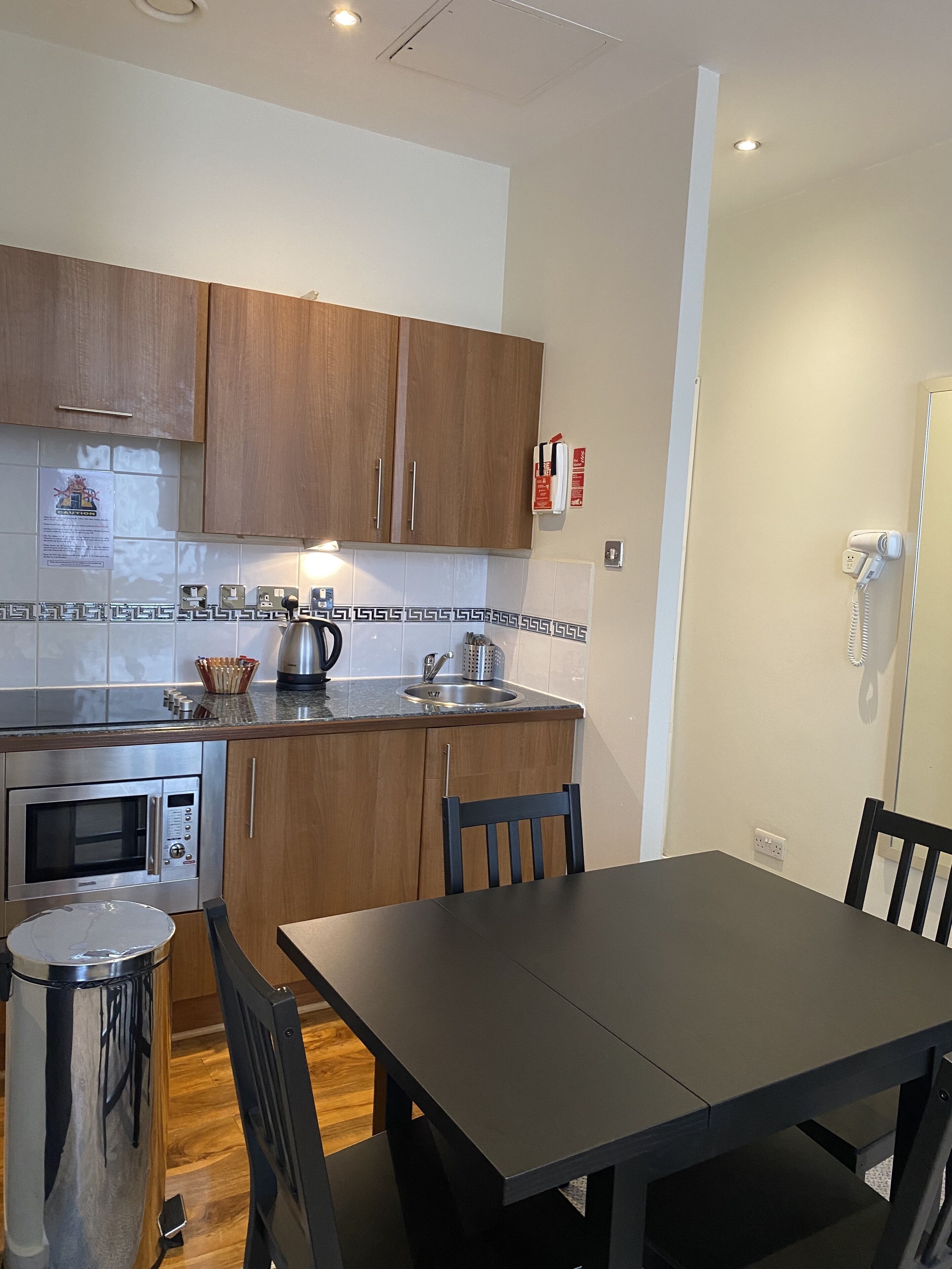 A modern kitchen with wooden cabinets, a stainless steel oven, and a sink. There is a dining table with chairs and a trash can.