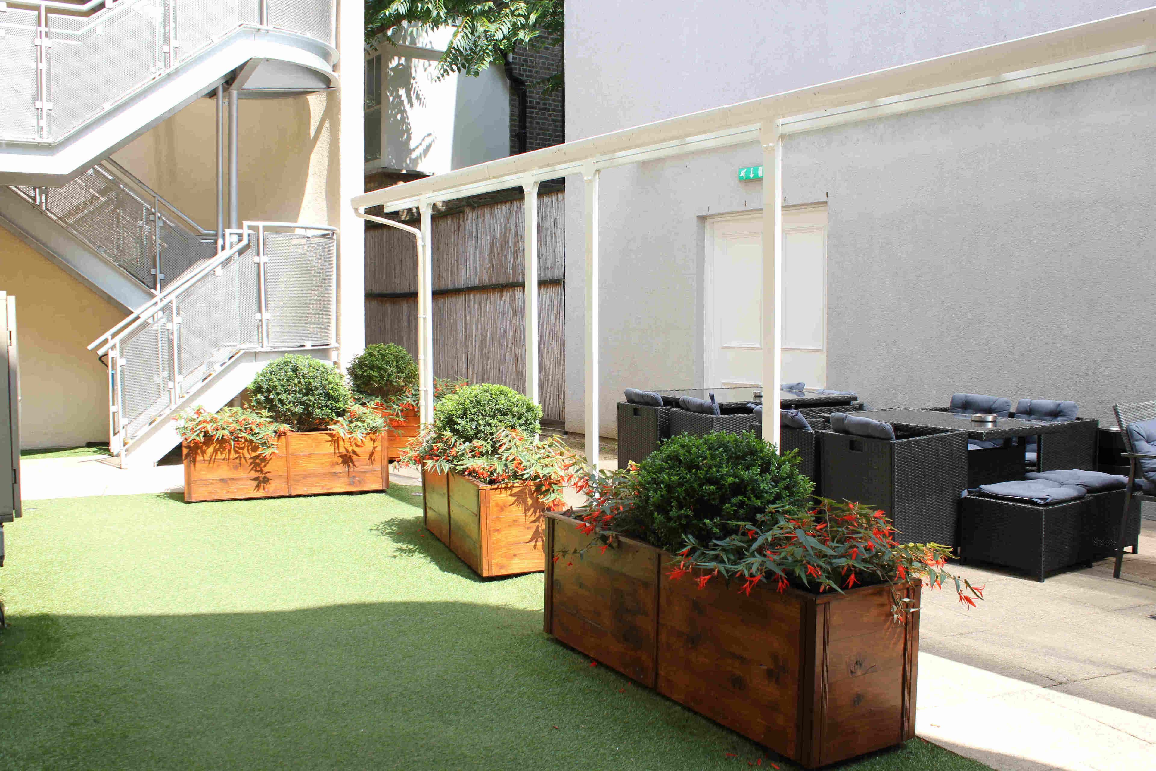 A courtyard with artificial grass, wooden planters with greenery, outdoor seating, and a staircase.