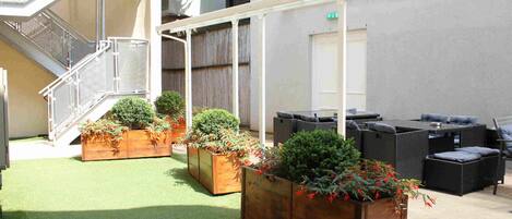 A courtyard with artificial grass, wooden planters with greenery, outdoor seating, and a staircase.