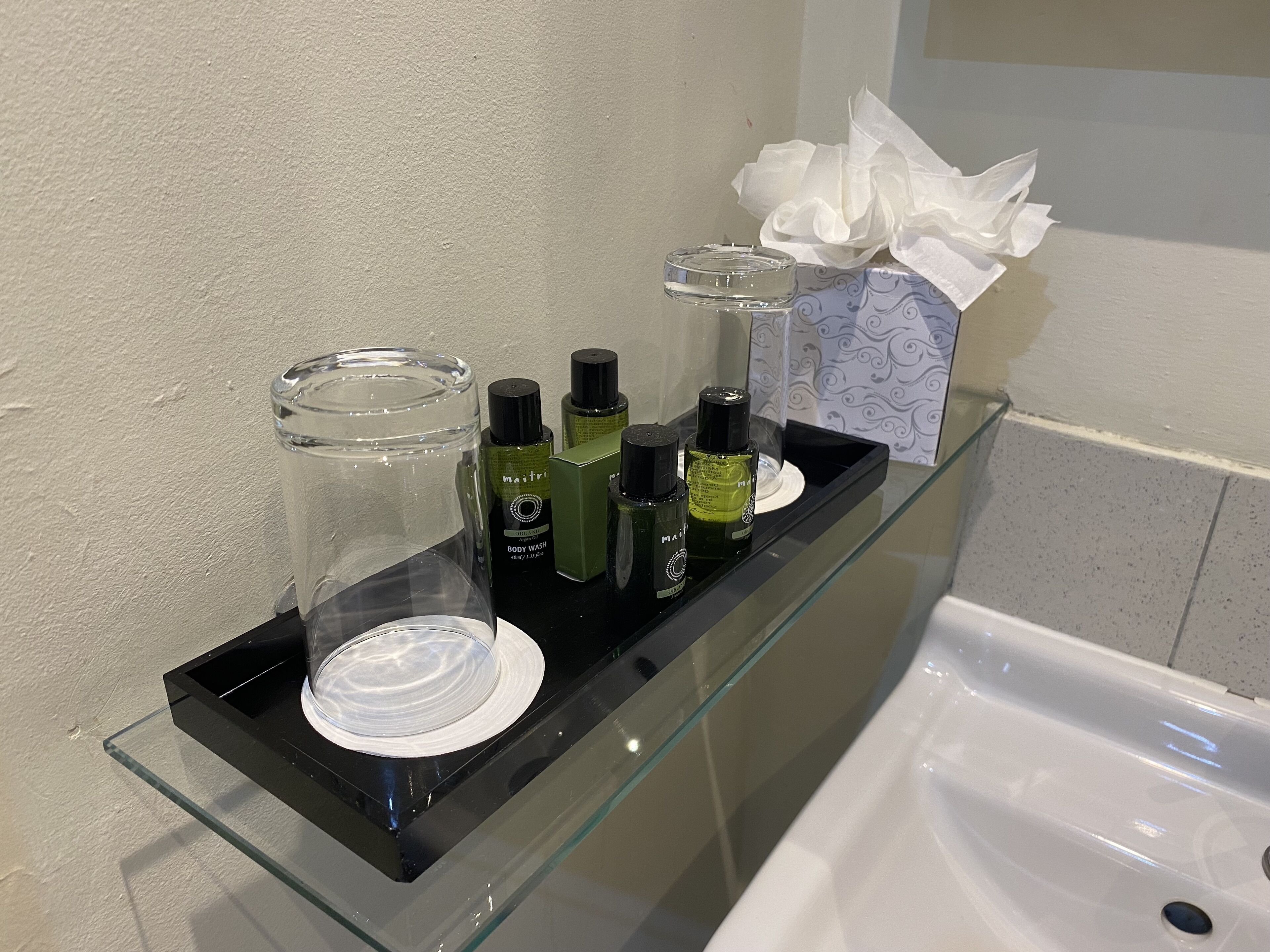 Ein Badezimmer-Waschtisch mit einer Glasablage, auf der verschiedene Pflegeprodukte liegen, darunter Duschgelflaschen und ein klares Glas.