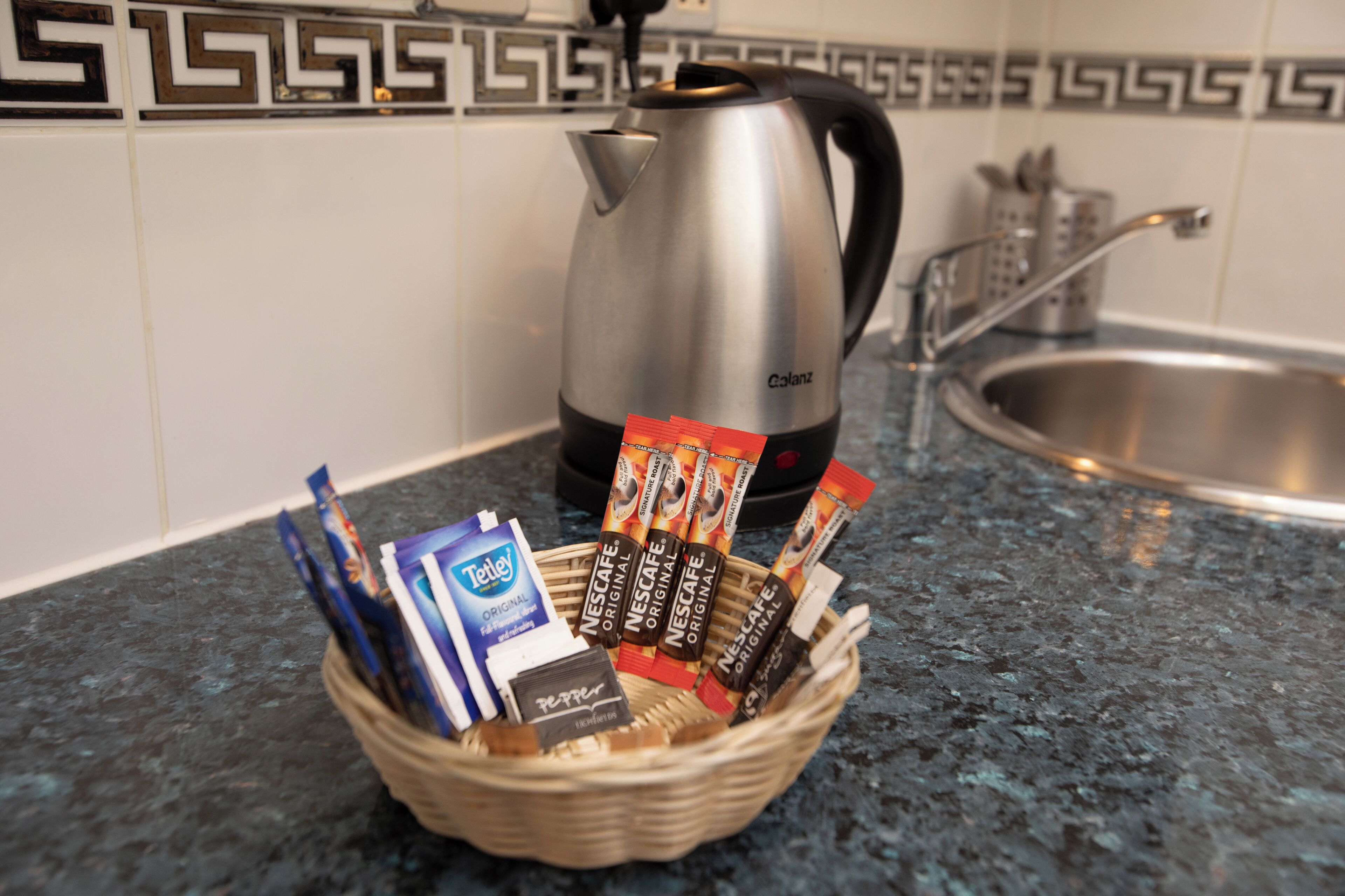 A kitchen counter with a stainless steel kettle, a basket of coffee pods, and a Nespresso machine.