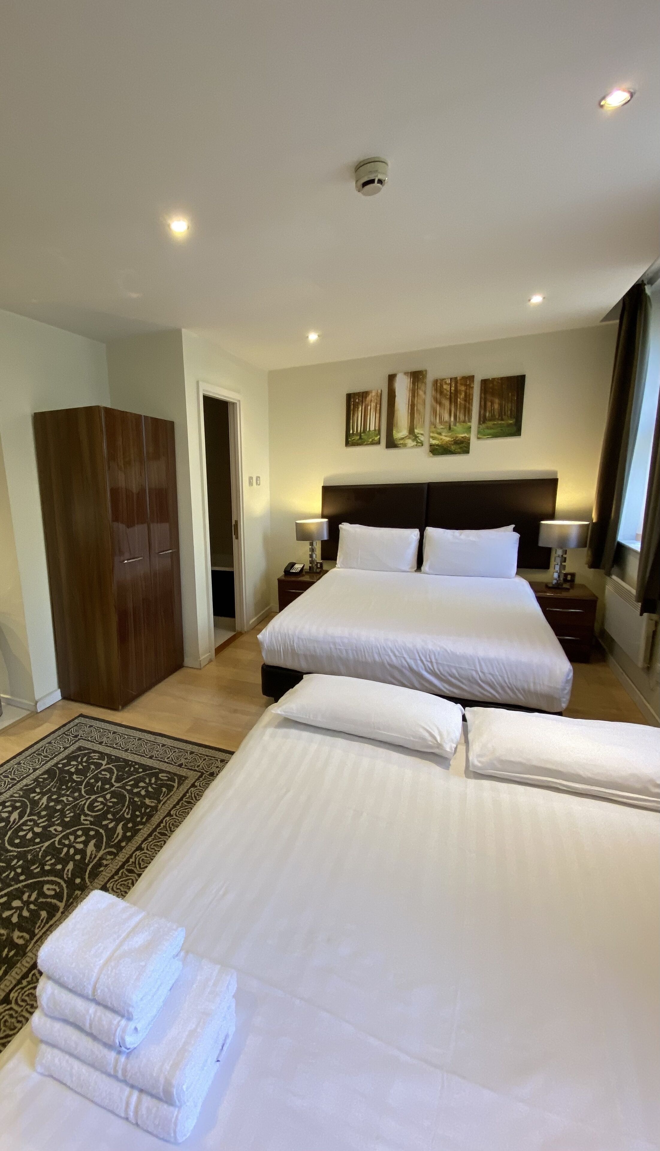 A hotel room with a large bed, two bedside tables with lamps, a wardrobe, and a door leading to another room.