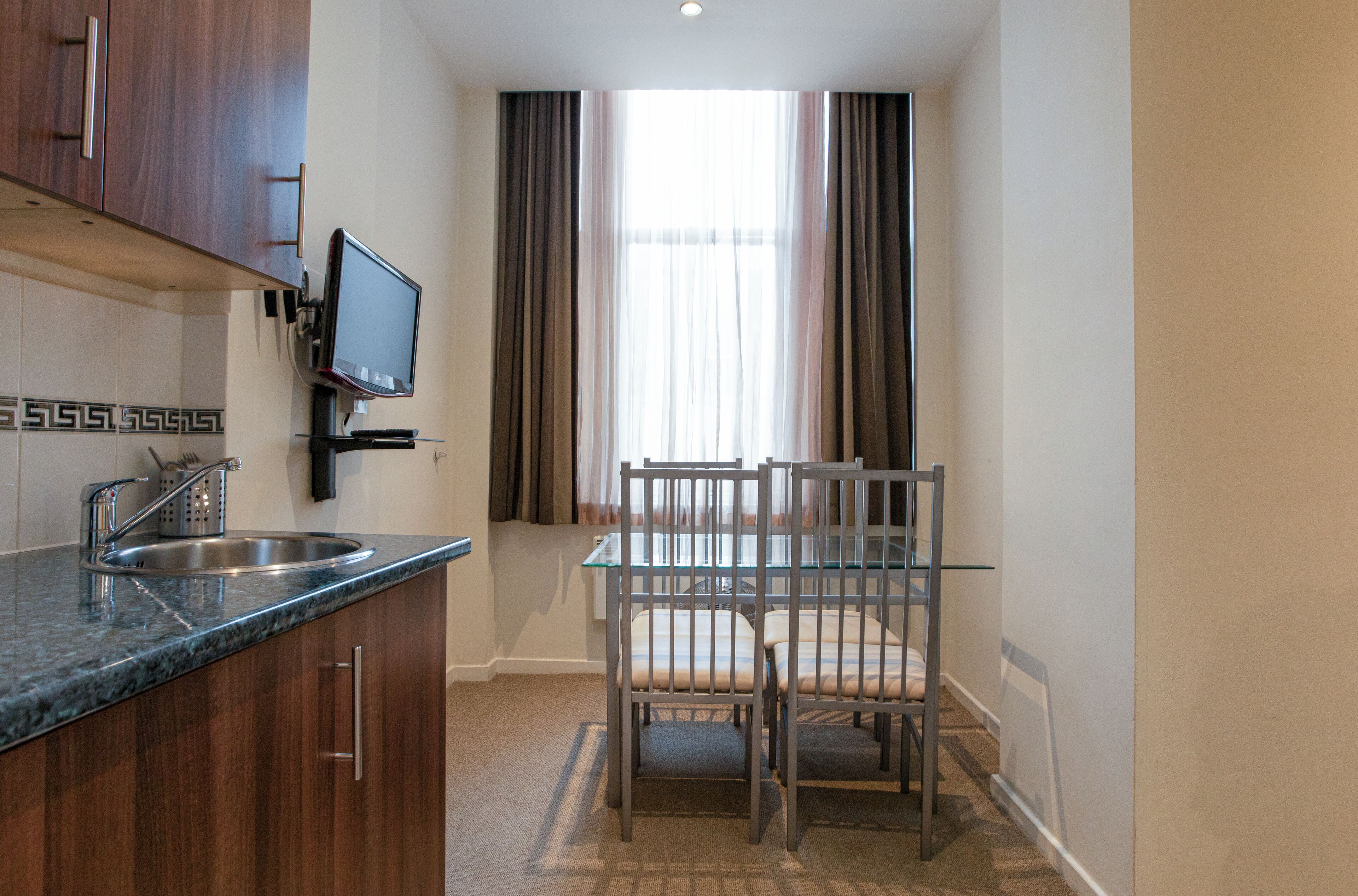 A compact kitchen with a built-in TV, a sink, and a dining area with a glass table and chairs.