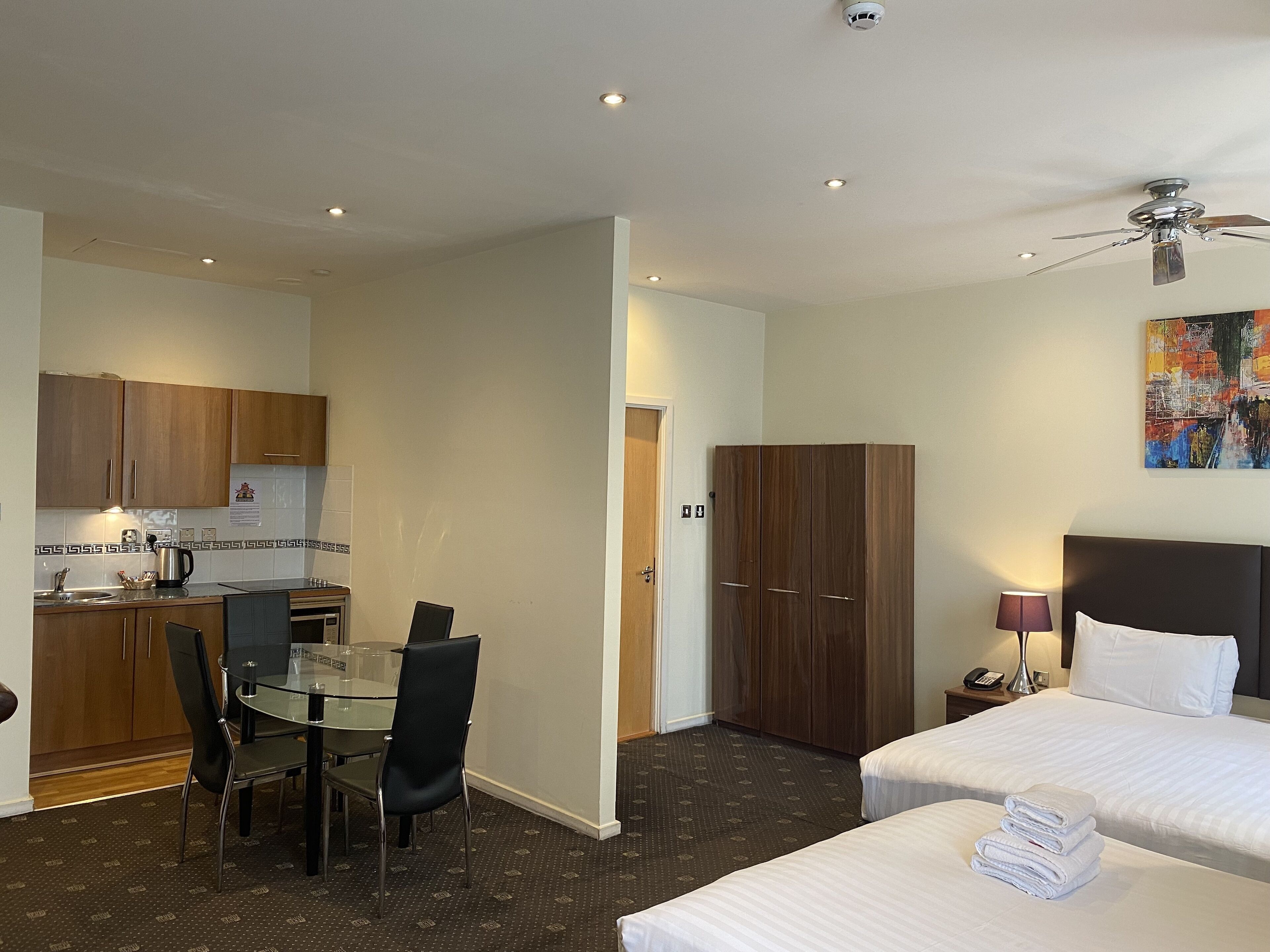 Une chambre d’hôtel comprenant un lit, un bureau avec une chaise, une kitchenette et une armoire.