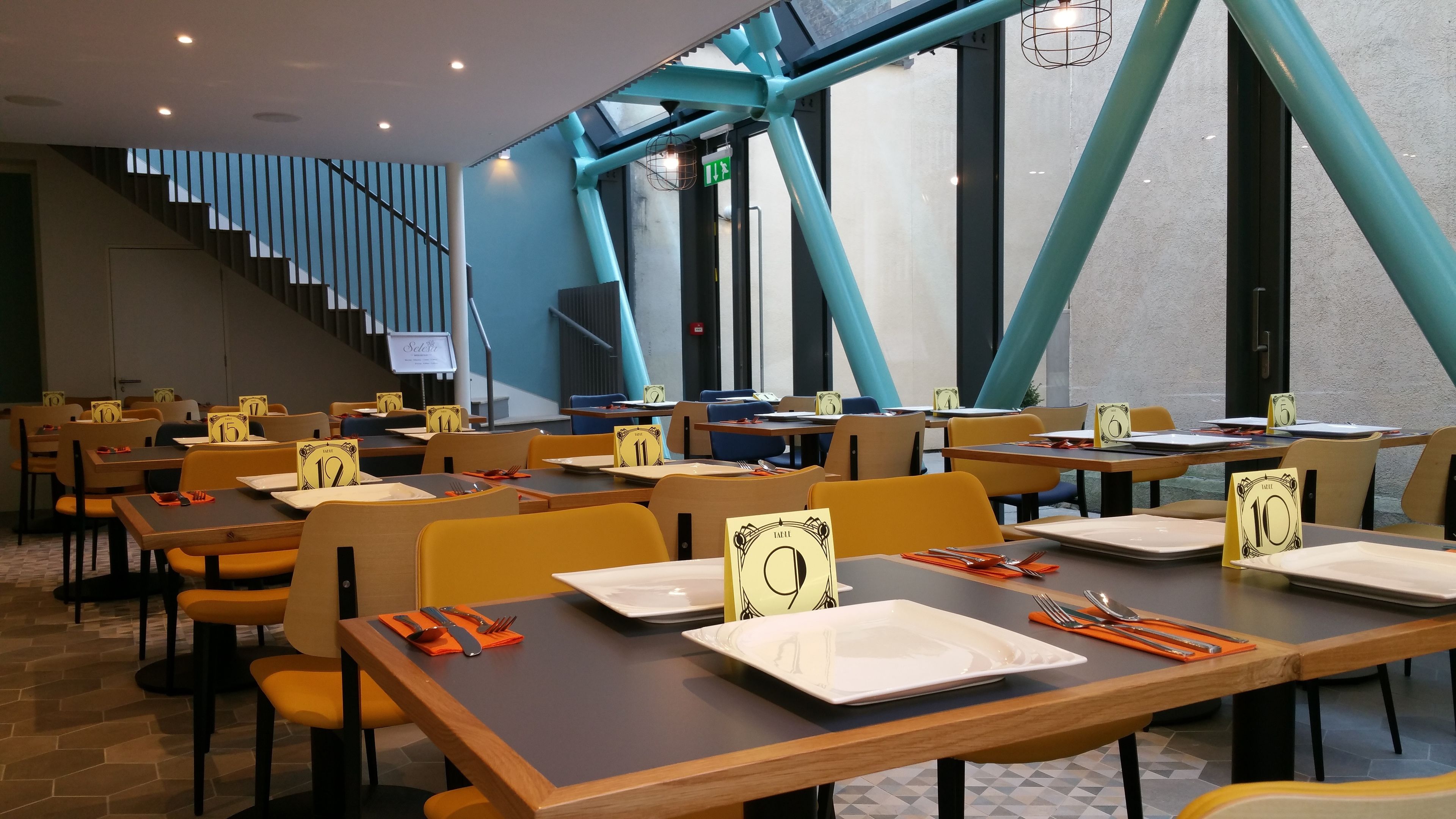 A modern dining area with tables numbered for reservation, a staircase, and a view of the outdoors.