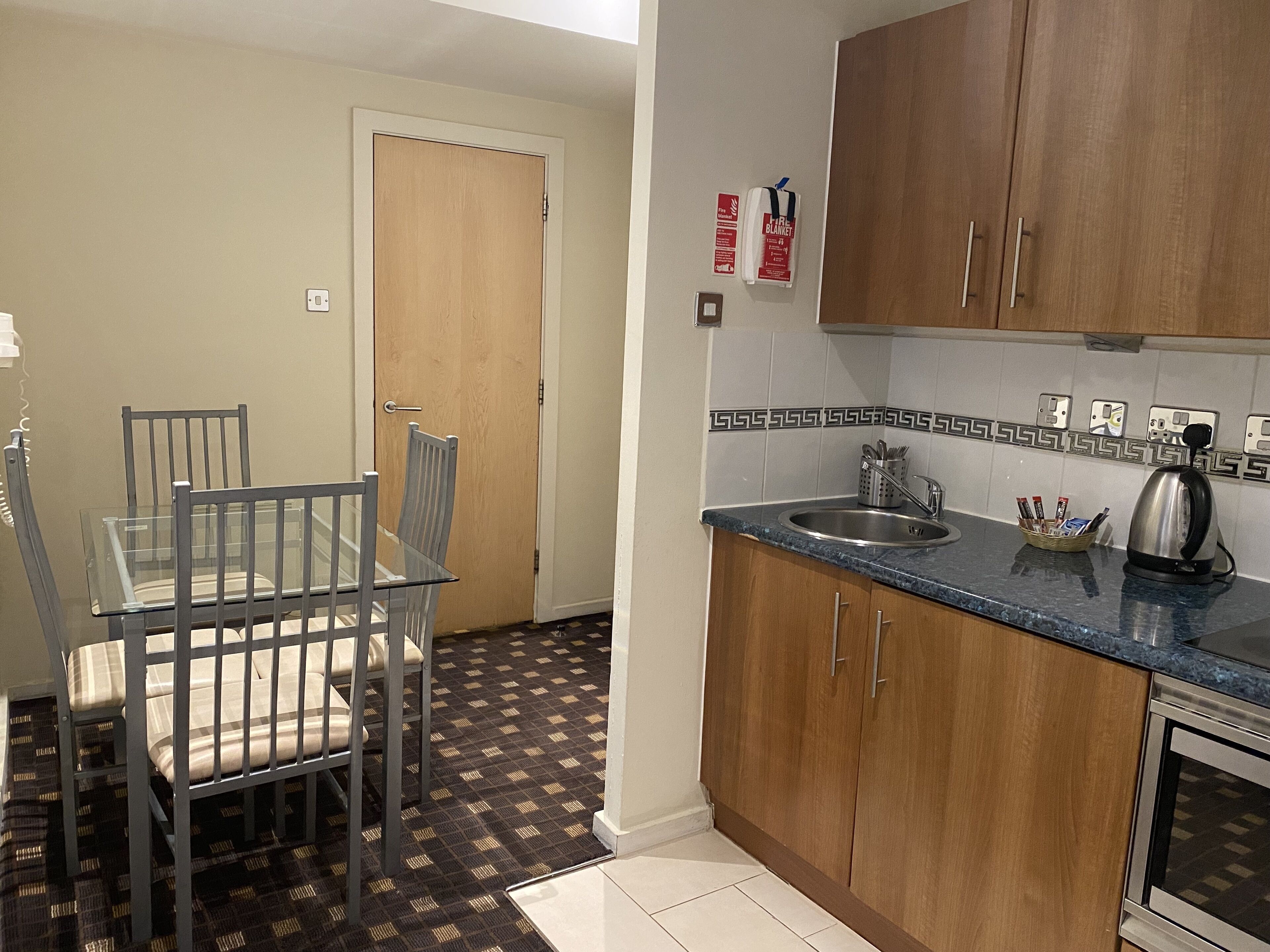 A compact kitchen with wooden cabinets, a sink, and a kettle.