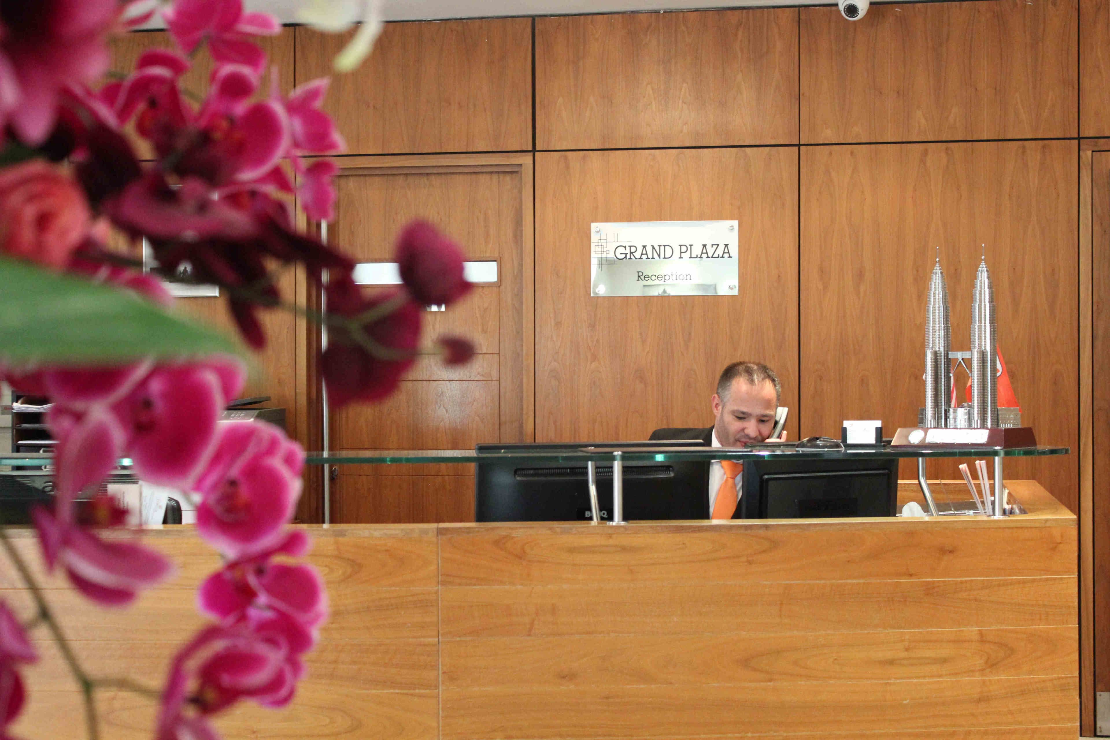 A reception desk with a sign reading "Grand Plaza Reception" and a model of the Petronas Towers.