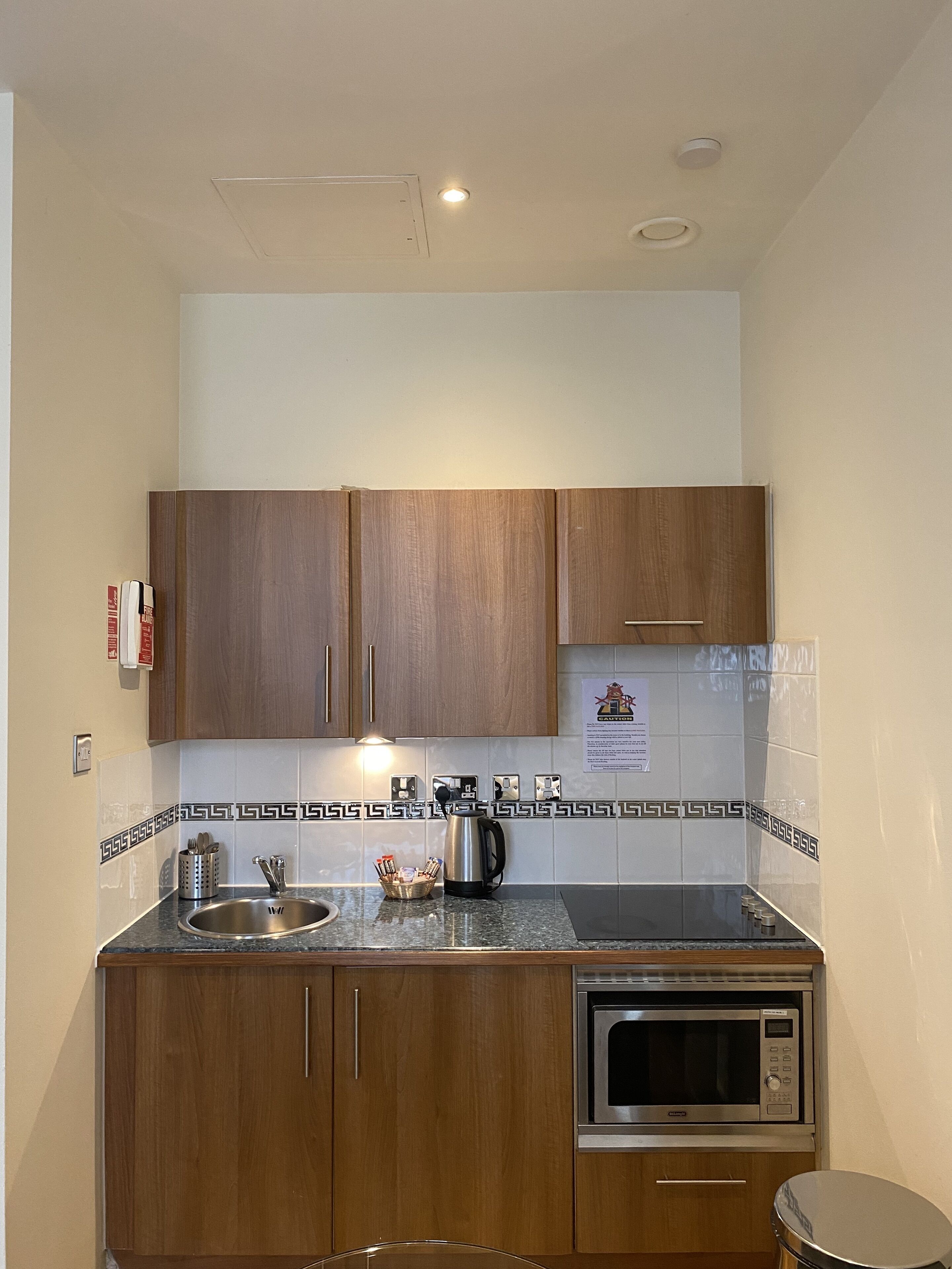 A compact kitchen with wooden cabinets, a stainless steel sink, a microwave, and a kettle.