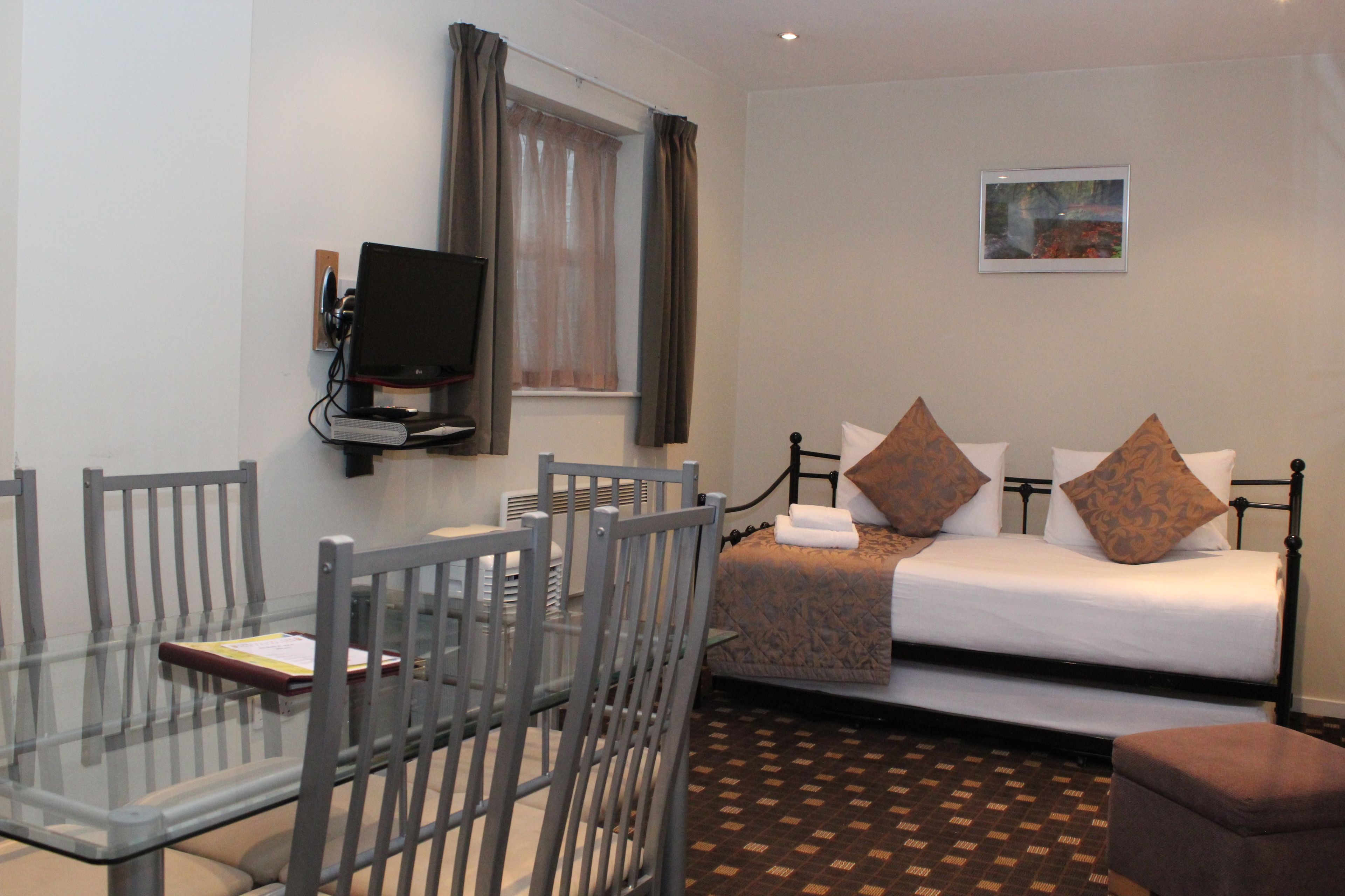 A hotel room with a bed, a desk with chairs, a television, and a window with curtains.