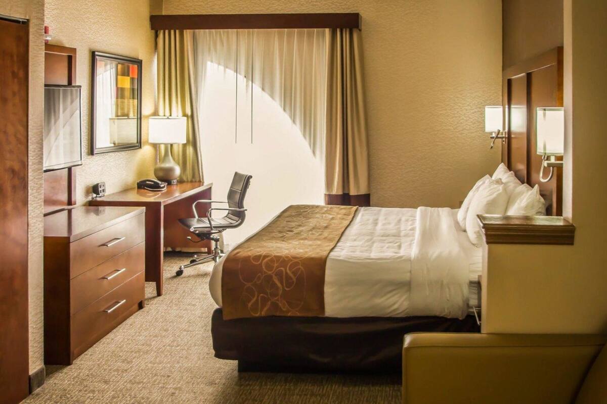 Hotelkamer met een bed, bureau, stoel, lamp, spiegel en raam met gordijnen.