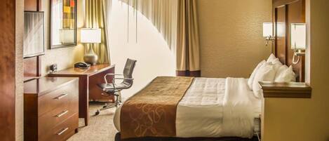 A hotel room with a bed, a desk, a chair, a lamp, a mirror, and a window with curtains.