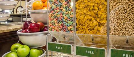 Una barra de desayuno con diversas opciones de comida, como manzanas, naranjas y cereales.