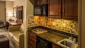 Cocina de hotel compacta con microondas, estufa, fregadero y un original mosaico en la pared.