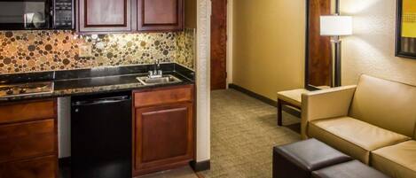 Una habitación de hotel compacta con kitchenette, un sofá y una pequeña mesa.
