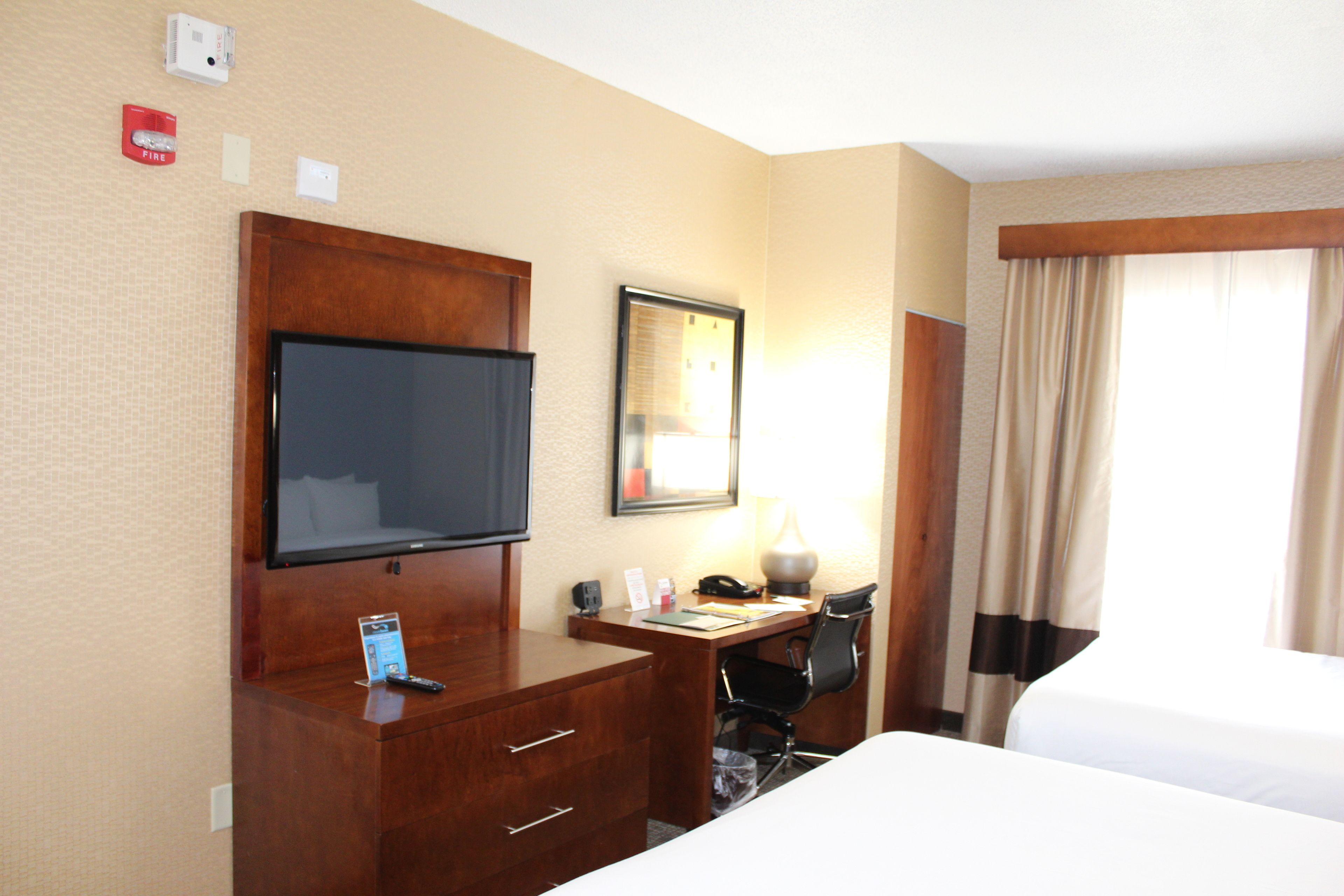 Habitación de hotel con televisión, escritorio, silla, lámpara y cama.