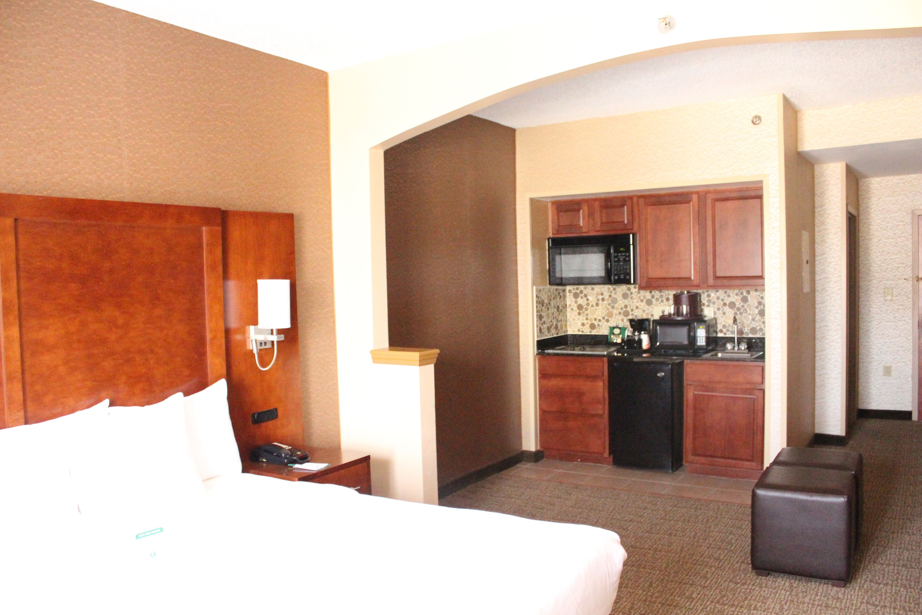 A hotel room with a bed, a desk, a telephone, and a kitchenette with a microwave and stove.