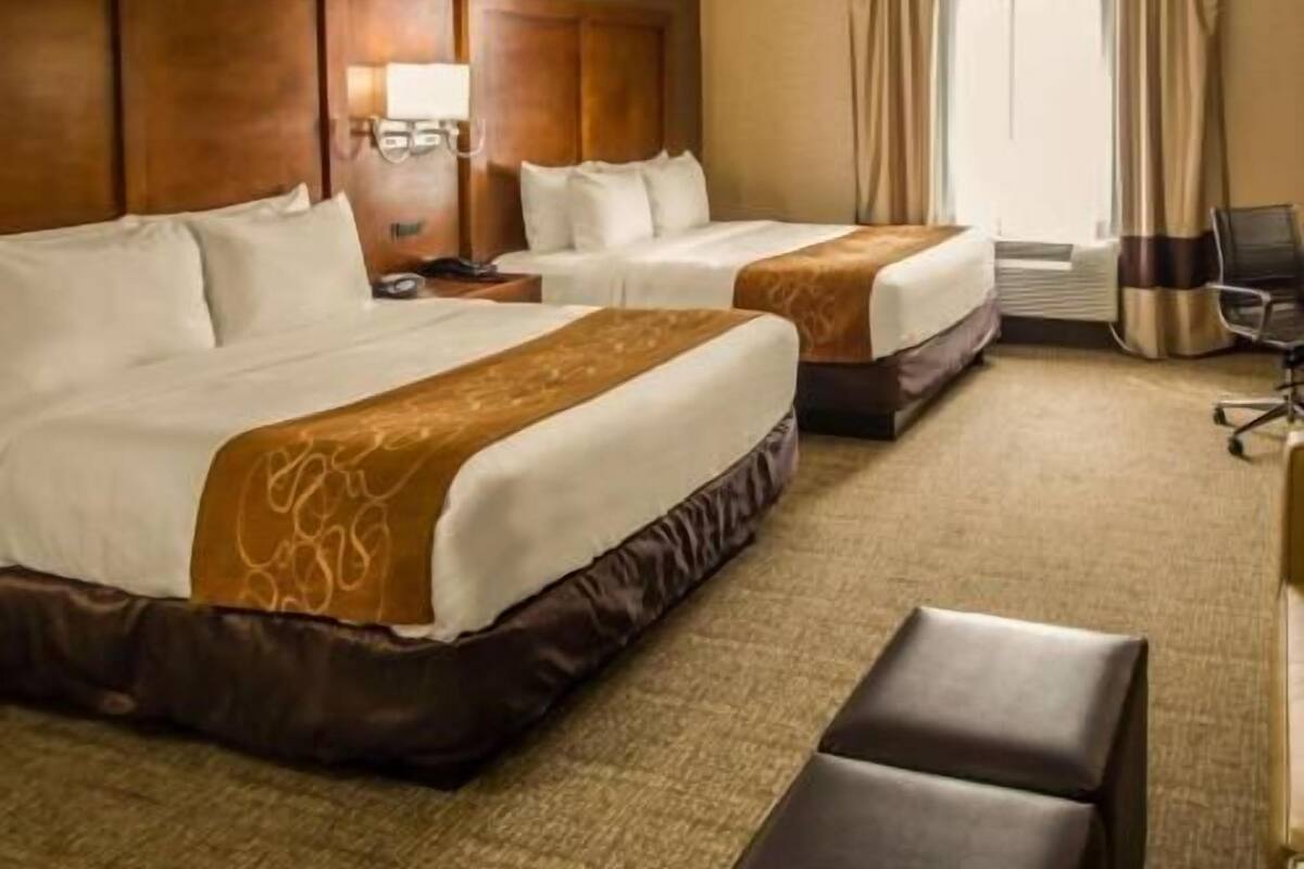 Een hotelkamer met twee bedden, een bureau, een stoel en een raam met gordijnen.