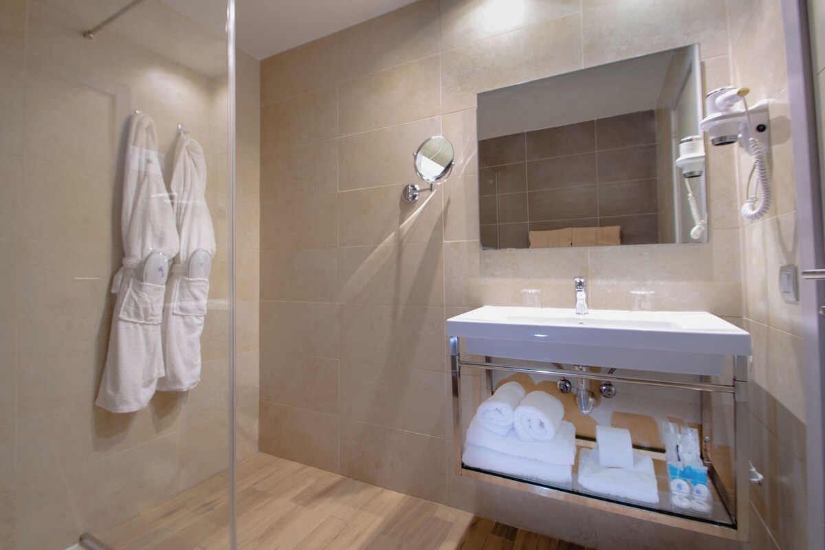 A modern bathroom with a glass shower enclosure, a built-in sink with a mirror, and a towel rack with robes.