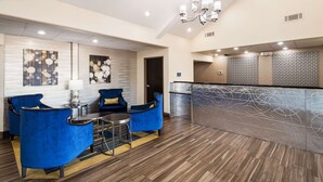 A lobby with blue armchairs, a small table with a lamp, and a reception desk with a patterned backdrop. - Best Western Plus Tulsa Inn & Suites (Tulsa)