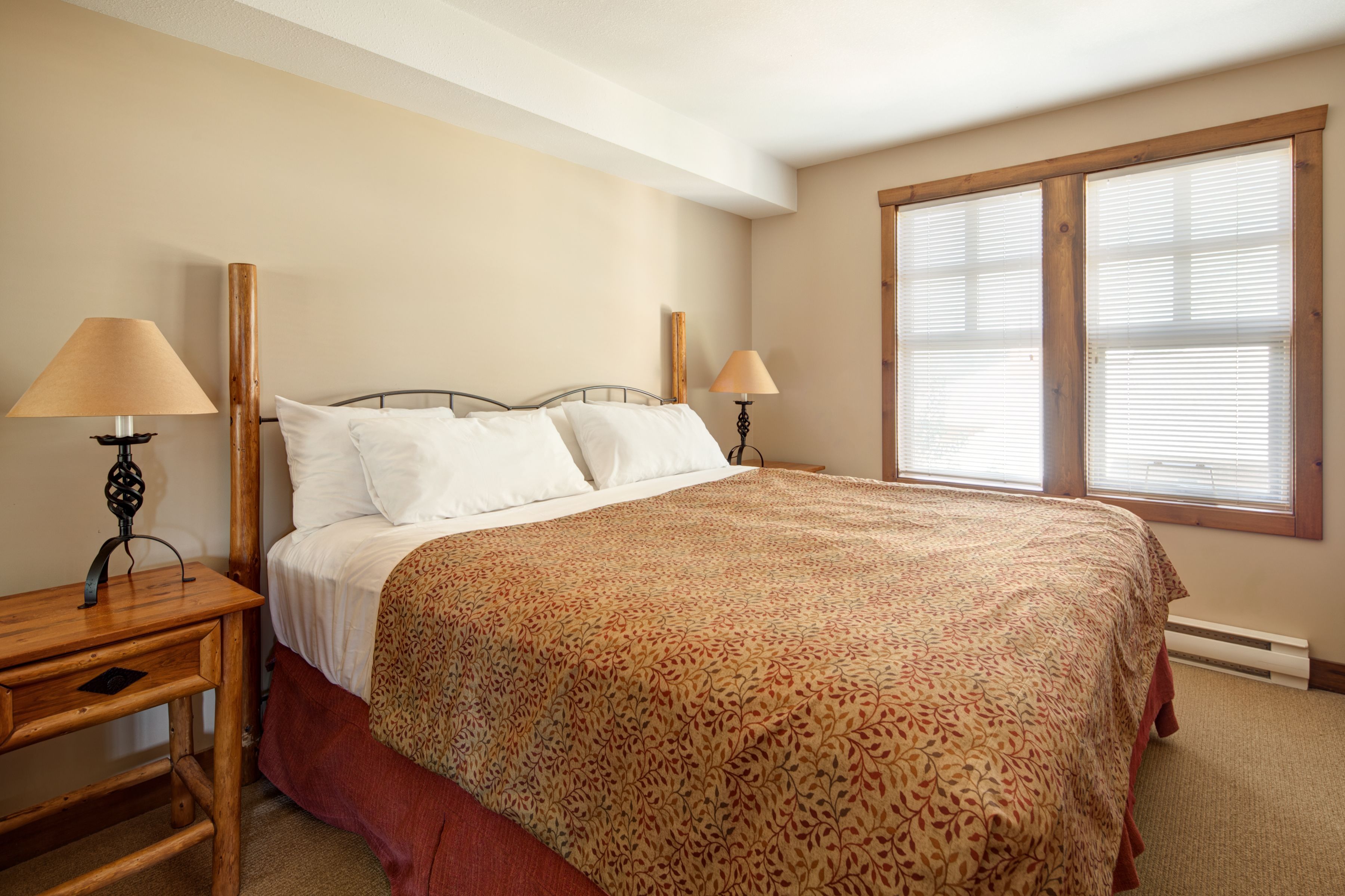 A bedroom with a large bed, two bedside tables, and a window with blinds.