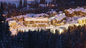 Een besneeuwde lodge met meerdere gebouwen, een skilift op de achtergrond en een goed verlicht centraal gebied.