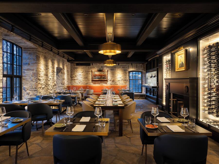 Ein Restaurant mit Steinwänden, Holzbalken und einem Weinkühlschrank. Die Tische sind mit Weingläsern und Tellern gedeckt.