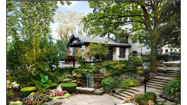 Un bâtiment traditionnel en pierre, doté d’un toit en pente, entouré d’un jardin bien entretenu où poussent diverses plantes et où se trouve une petite cascade.