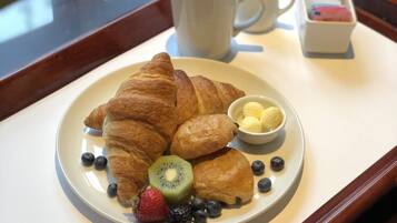 A tray with a plate of croissants, blueberries, strawberries, kiwi, and a small bowl of butter. There are also two cups of coffee and a small container of sugar cubes.