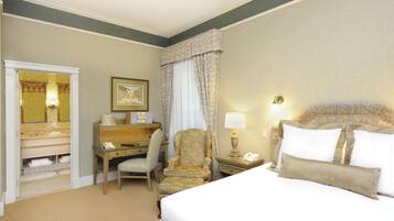 A hotel room with a bed, a desk with a chair, a vanity with a mirror, and a nightstand with a lamp.
