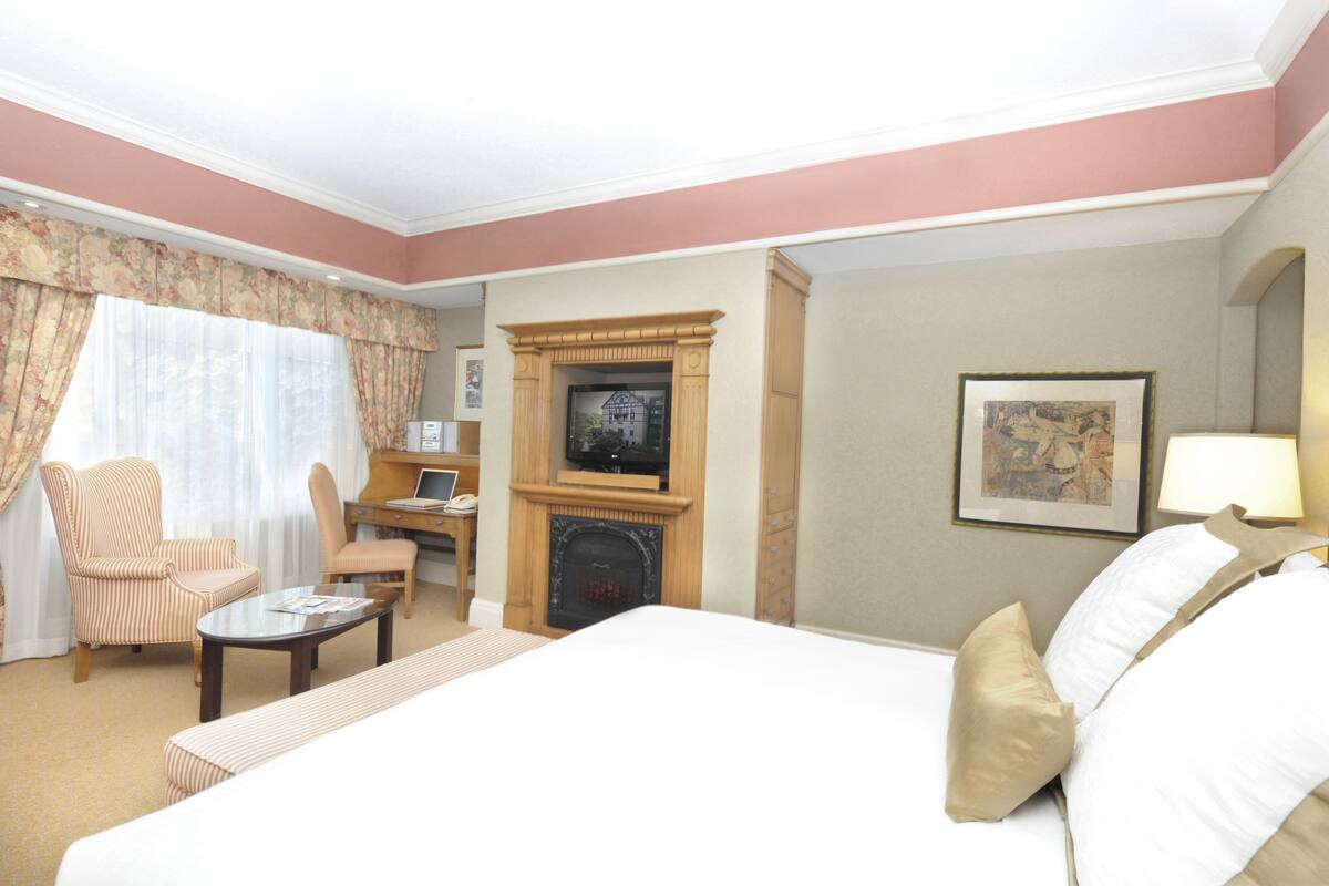 Hotelkamer met een bed, televisie, open haard, bureau met stoel en raam met gordijnen.