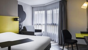 A hotel room with a bed, two chairs, a desk, a lamp, and a large window with sheer curtains. - ibis Styles Nice Vieux Port (Nice)