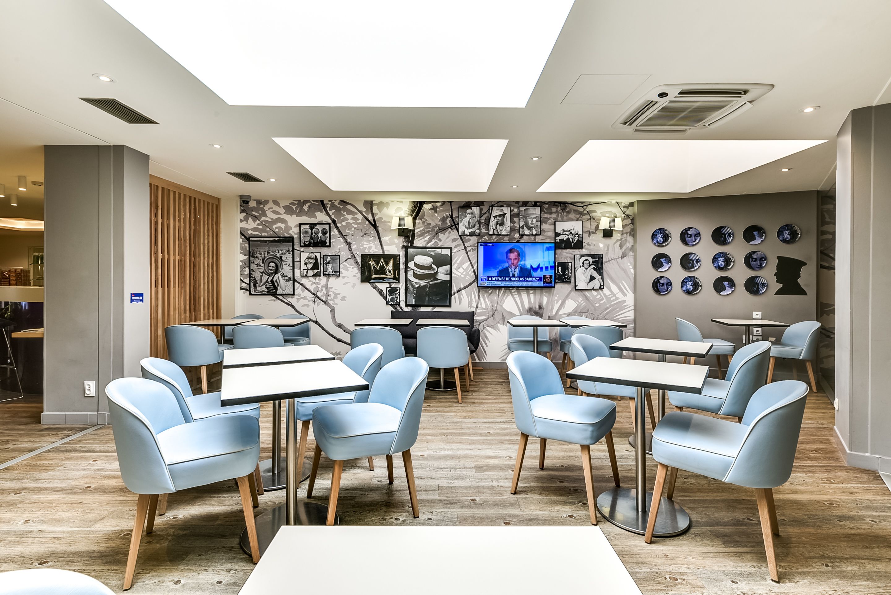 Un comedor moderno con sillas y mesas azul claro, una pantalla de televisión y una pared decorada con fotos y platos enmarcados.
