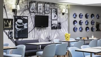 A modern interior with a seating area, tables, and a wall decorated with framed pictures and a flat-screen TV.
