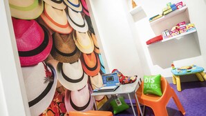 A children's play area with a wall of hats, a small table with toys, and orange chairs. - ibis Styles Nice Vieux Port (Nice)