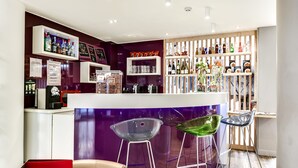 A bar area with a counter, stools, and shelves of bottles and glasses. - ibis Styles Nice Vieux Port (Nice)