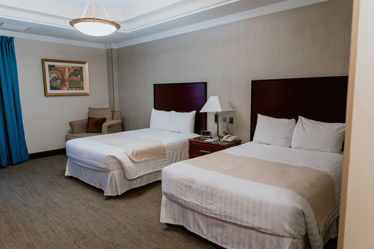 A hotel room with two single beds, a desk, a chair, a lamp, and a painting on the wall.