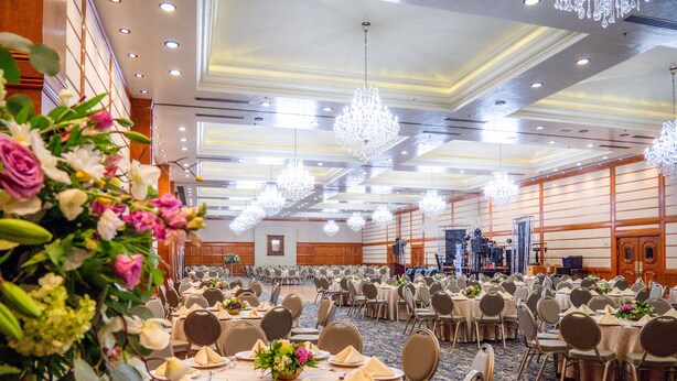 Un salón de banquetes con mesas redondas dispuestas para comer, sillas y centros de mesa florales.