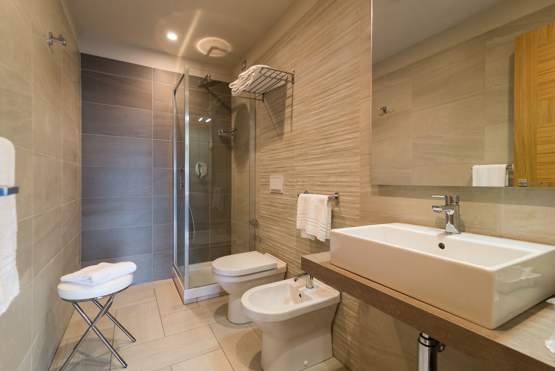 A modern bathroom with a glass-enclosed shower, a toilet, a bidet, and a large sink with a mirror.