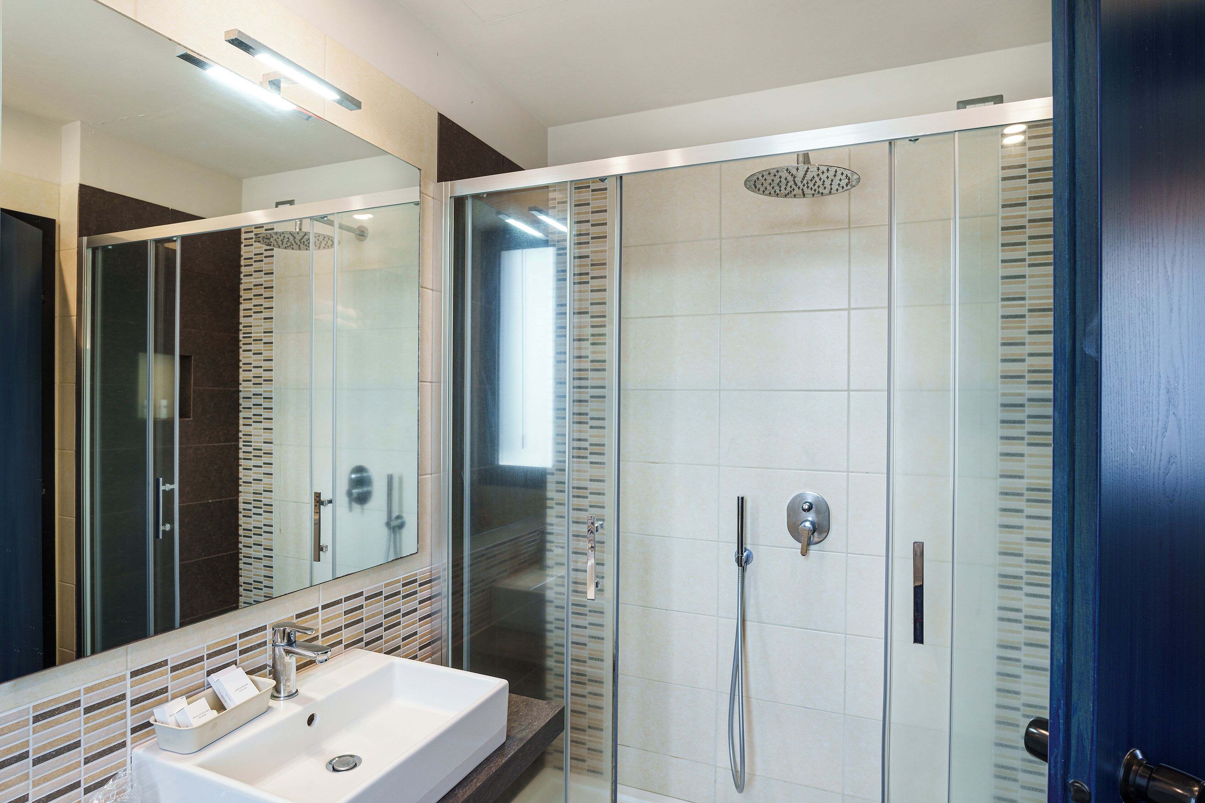A modern bathroom with a glass-enclosed shower, a large mirror, and a white sink.