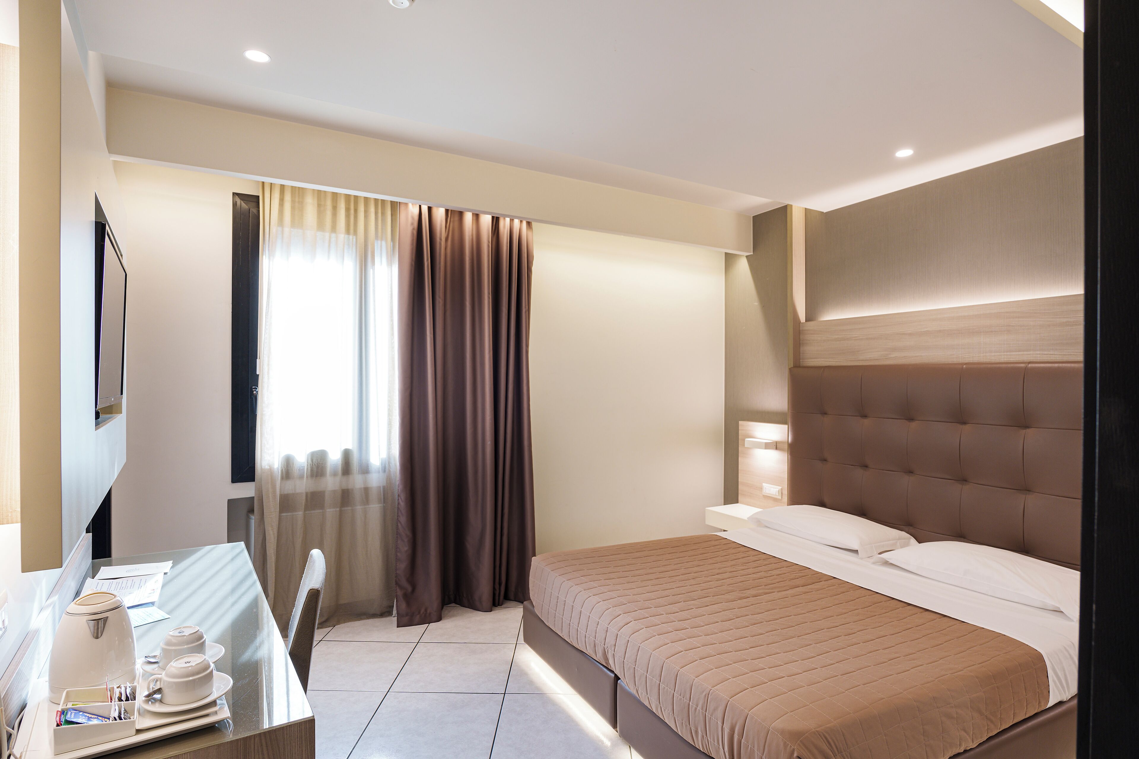 Ein Hotelzimmer mit Bett, Schreibtisch mit Stuhl, Fernseher und einem Fenster mit Vorhängen.