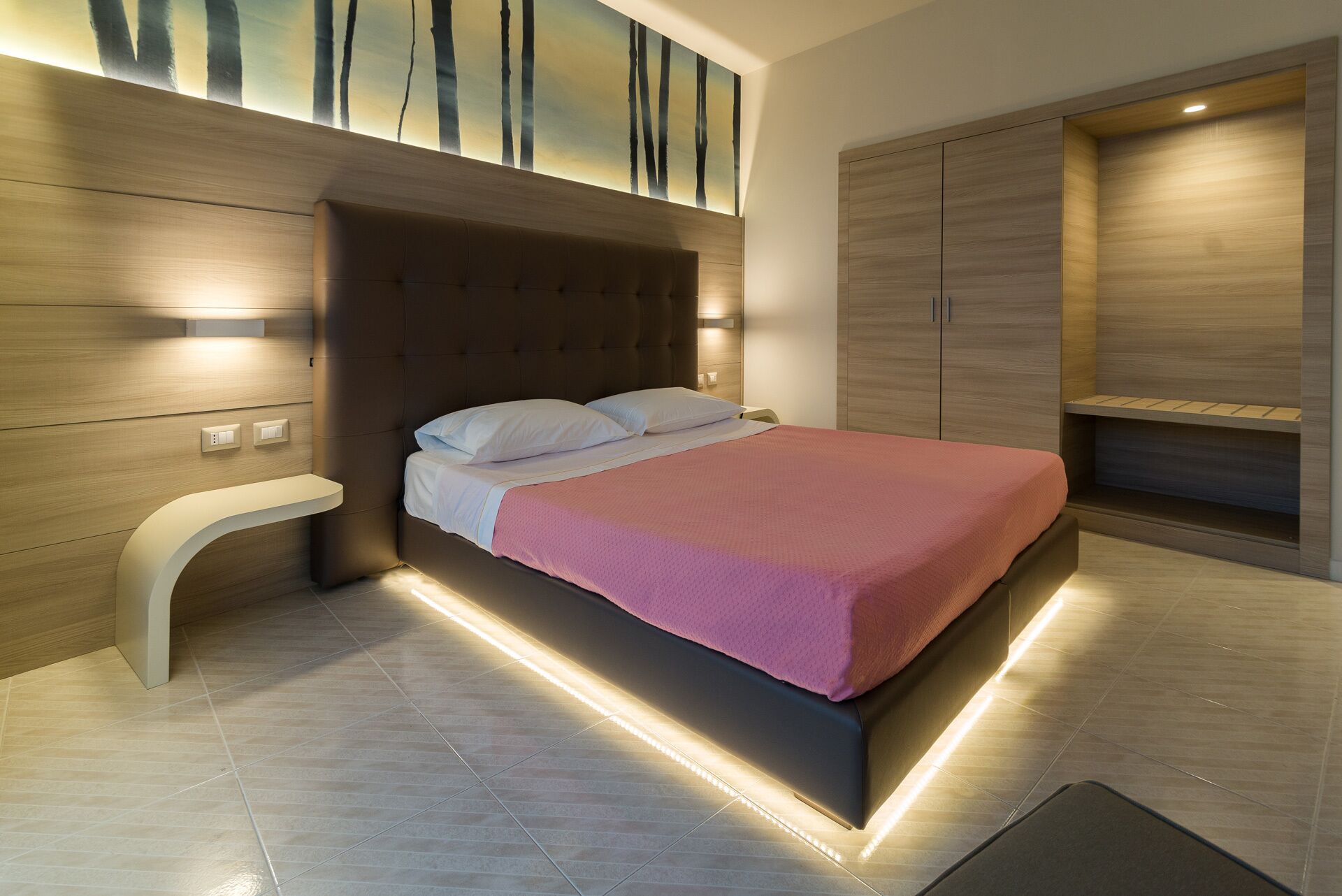 Una moderna camera da letto con un letto grande, poggiatesta integrato e illuminazione integrata.