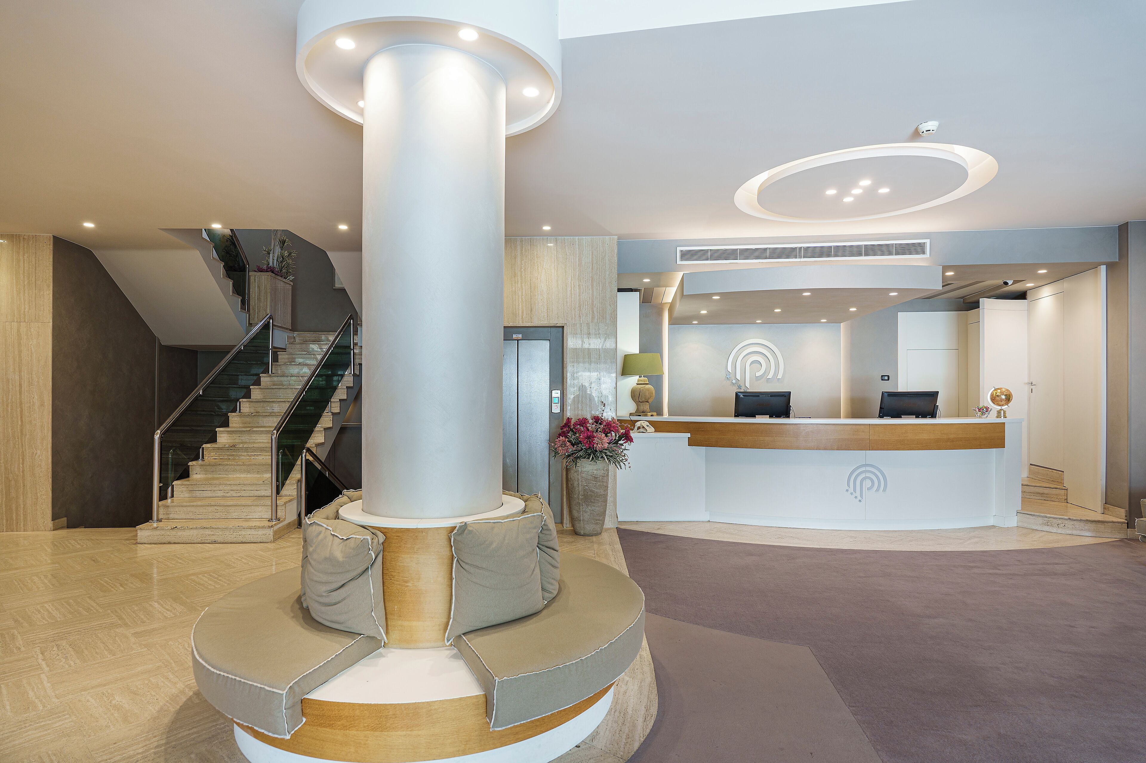 Un espace d’accueil moderne doté d’un pilier central, d’un comptoir de réception et d’un escalier.
