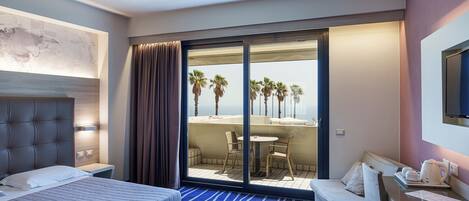 Una habitación de hotel con cama, escritorio, silla, sofá y balcón con mesa y sillas.