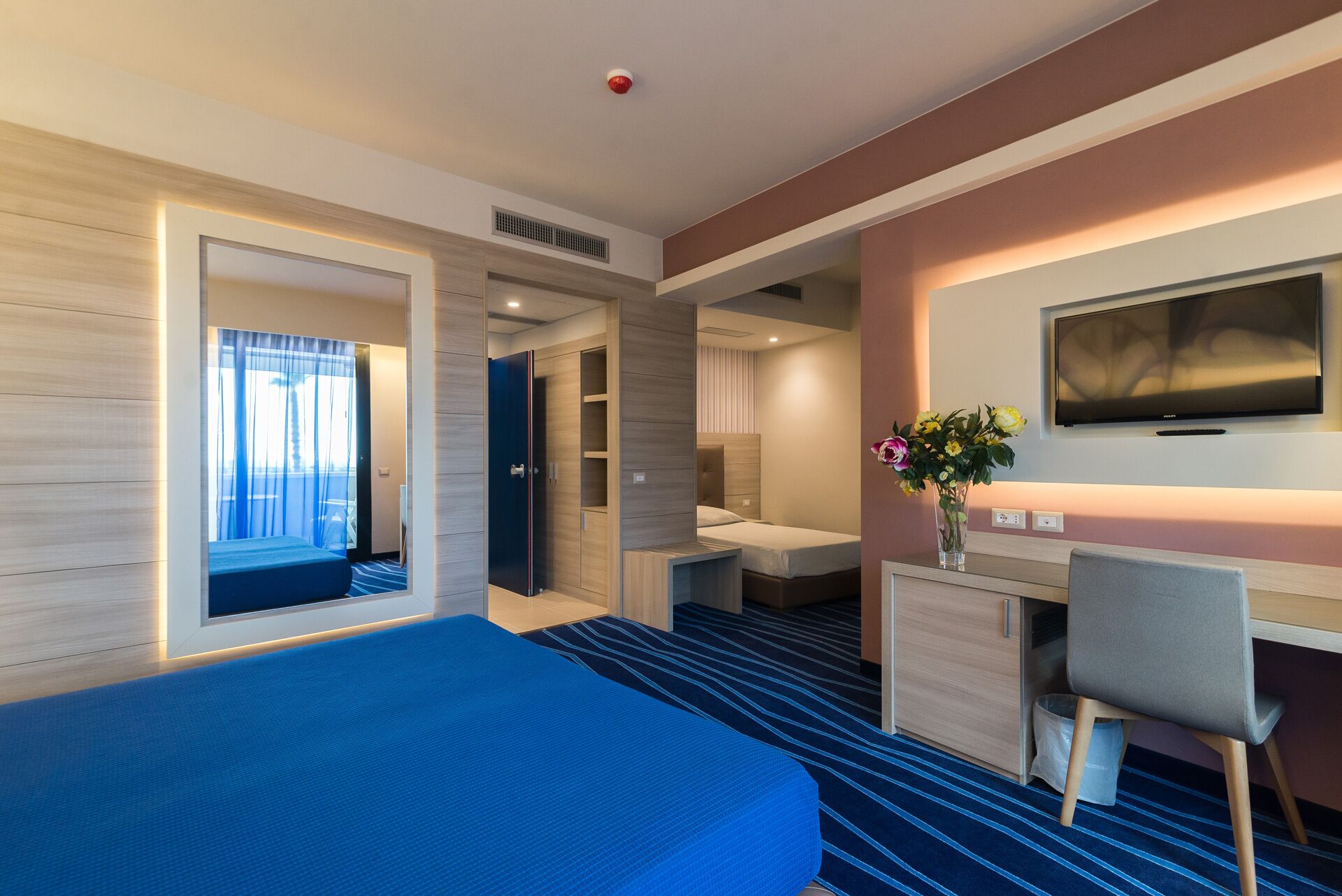 A hotel room with a bed, a desk, a chair, a TV, and a bathroom.