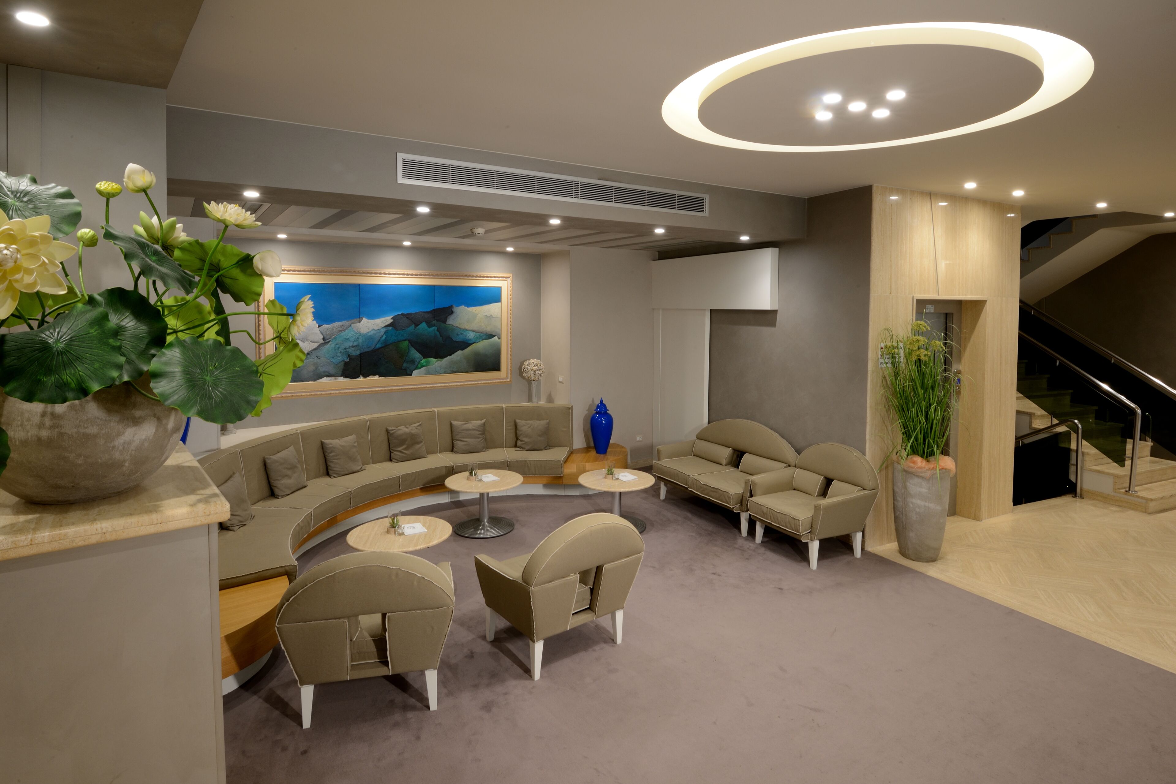 Un espace de détente moderne avec un canapé incurvé, des tables rondes et un grand tableau accroché au mur.