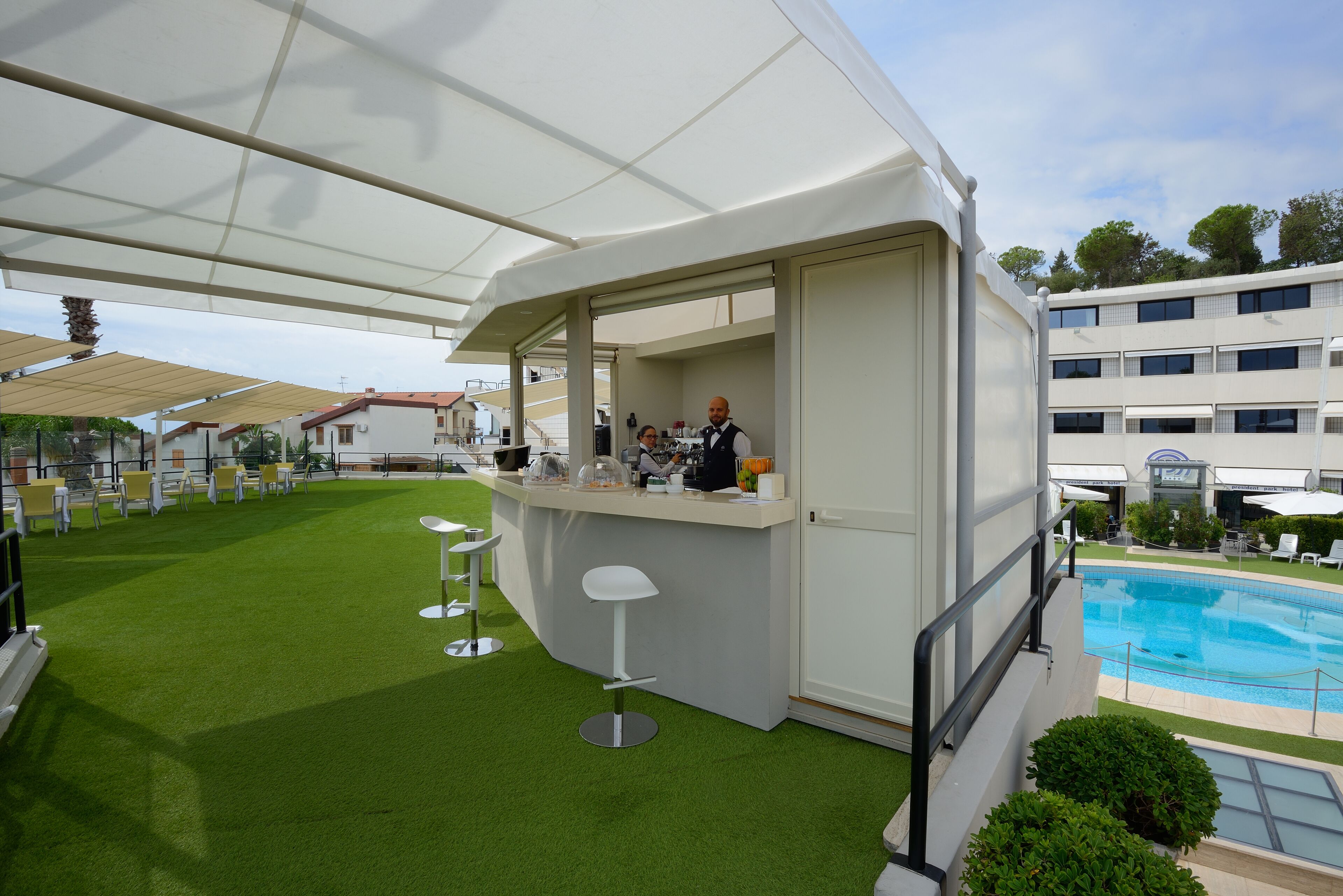 A poolside area with a bar, artificial grass, and a pool.