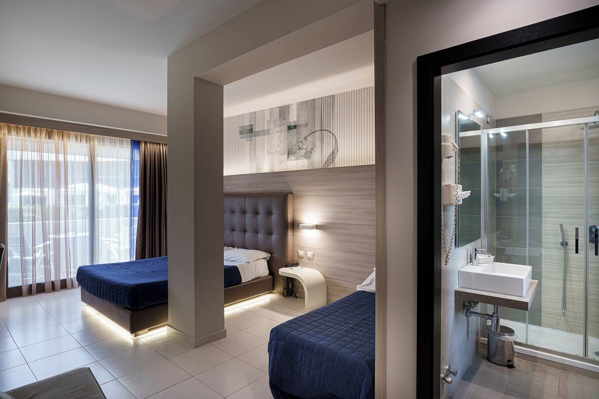 Een moderne hotelkamer met twee bedden, een badkamer en een groot raam met gordijnen.