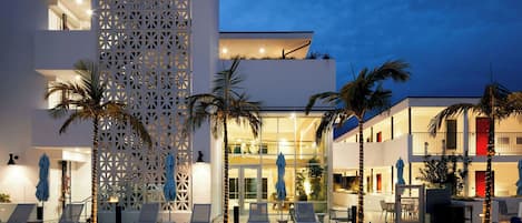 Un hôtel moderne doté d’une piscine, de chaises longues et de palmiers.